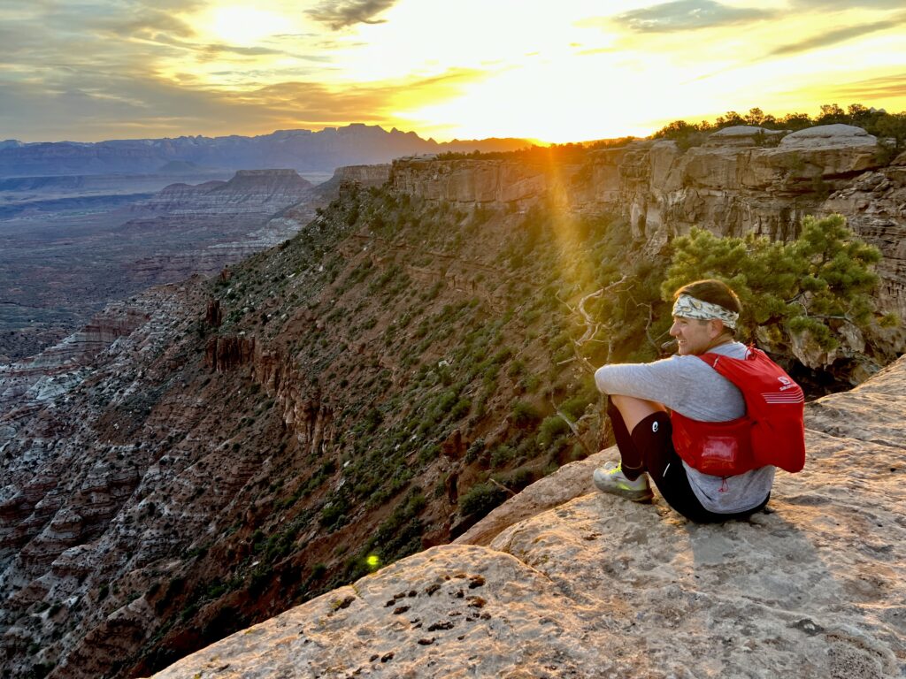 Alex Guglielmetti sitting on top of a cliff in Zion National Park at sunset.