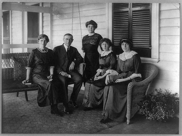 Woodrow Wilson, seated posed on swing on porch, facing front, with his wife and three daughters