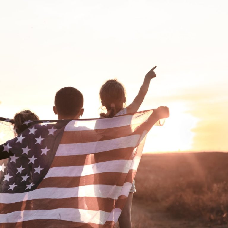 Three children hold an American flag behind them during a sunrise