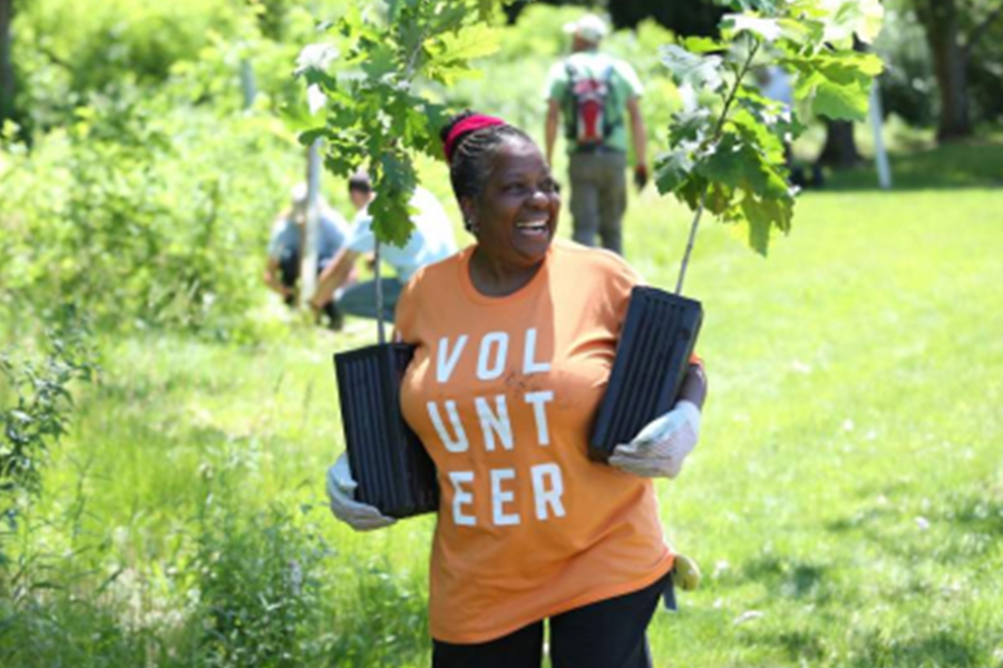 Volunteer smiles while holding tree saplings during a park cleanup and planting event.
