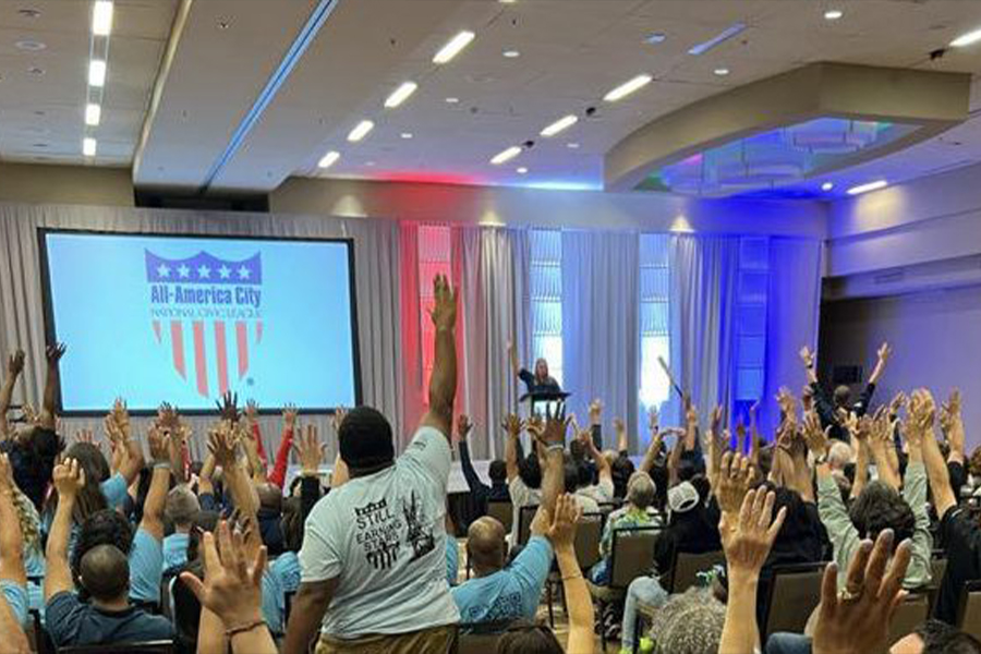 Community members raise hands at a civic engagement event celebrating volunteer-driven progress.