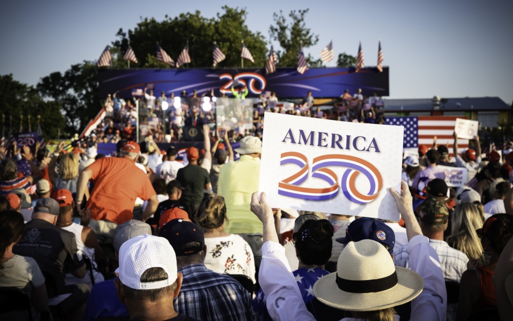 Woman holding America250 sign as President Trump gives speech at the America250 Iowa event on July 3 2025