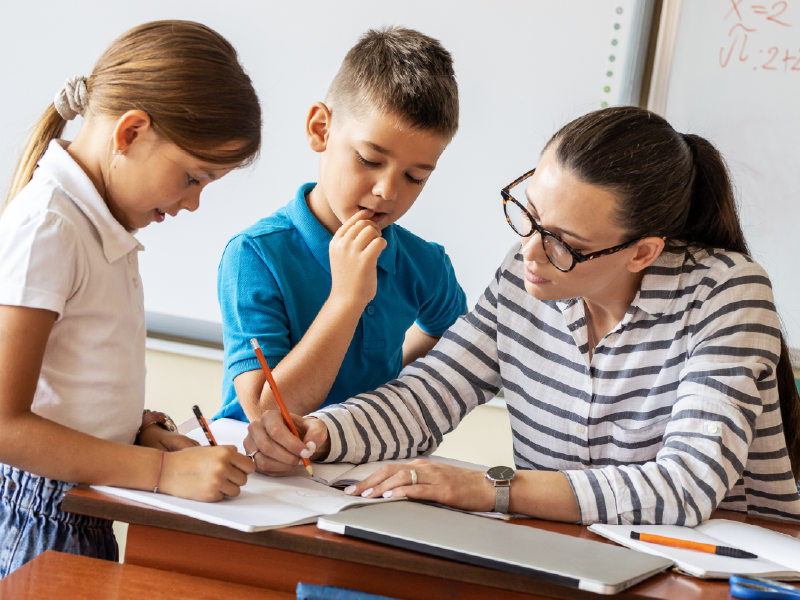 Teacher with two young students, writing in the notebook of one of the students